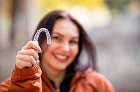 Happy young woman holding Invisalign clear aligner