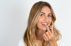 Smiling young woman holding Invisalign aligner close to her mouth