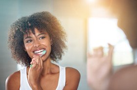 Woman brushing her teeth in front of bathroom mirror