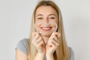 Happy young woman holding Invisalign aligners in heart shape