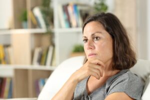 Woman sitting on sofa, wearing contemplative expression